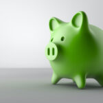A green piggy bank sits on a gray table against a gray wall to indicate affordable dental care