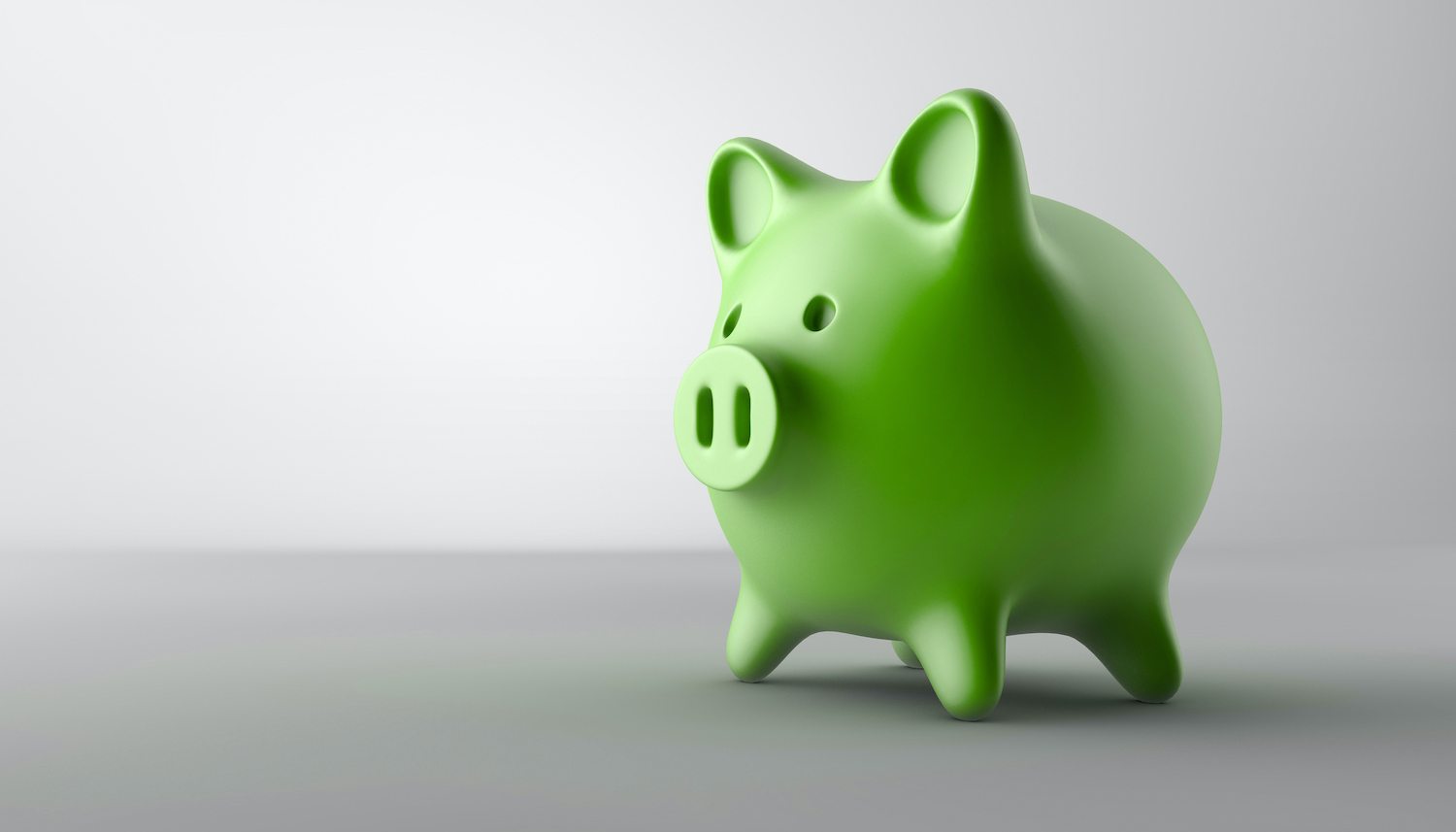 A green piggy bank sits on a gray table against a gray wall to indicate affordable dental care