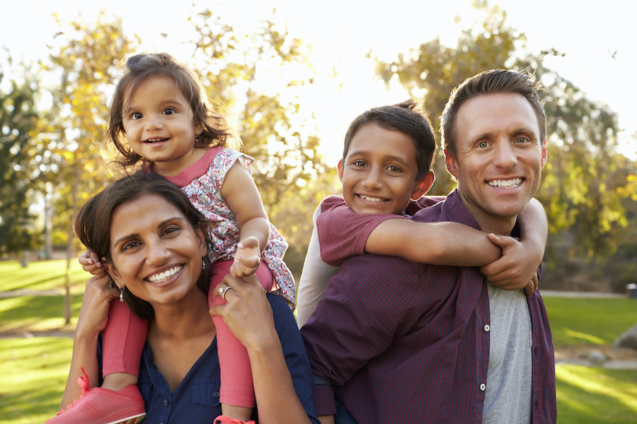 Mom and dad give piggyback rides to their son and daughter as they smile outside