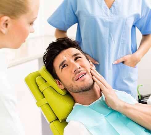 man sitting in a dental chair, holding his jaw in pain