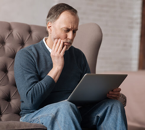 man holding his jaw in pain while looking at his laptop