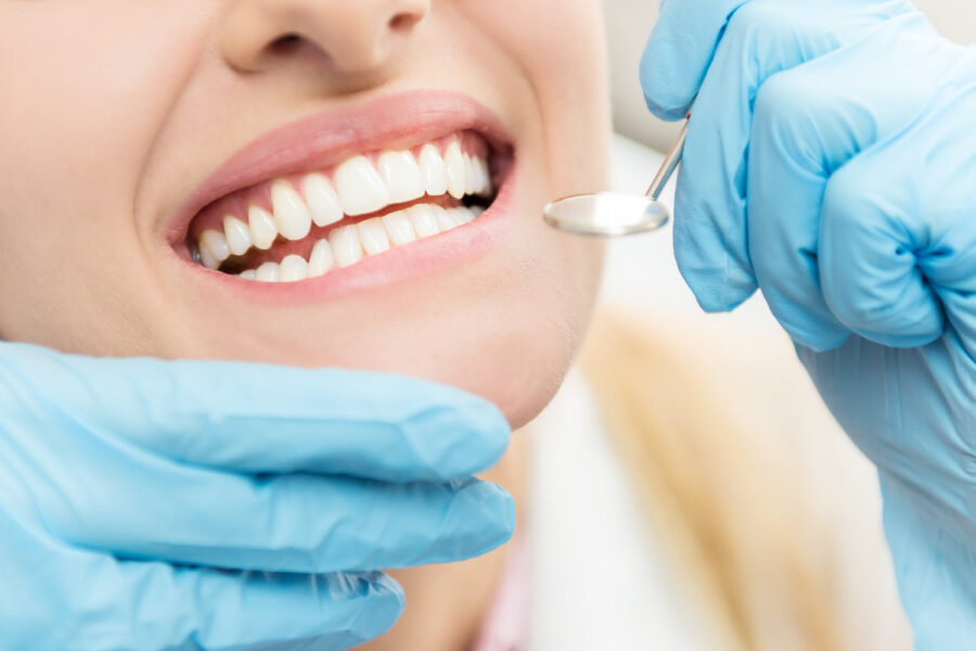 Closeup of a woman having her teeth examined at the dentist by a gloved hand holding a dental mirror